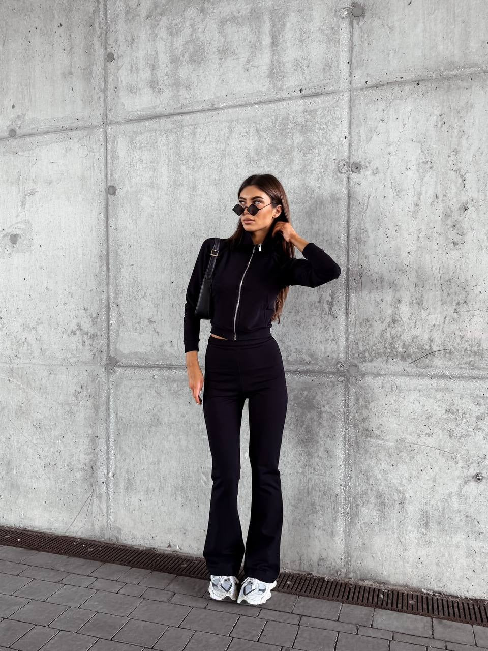 Czarny — komplet: krótka bluza na zamek i spodnie dzwony, cała sylwetka przy ścianie